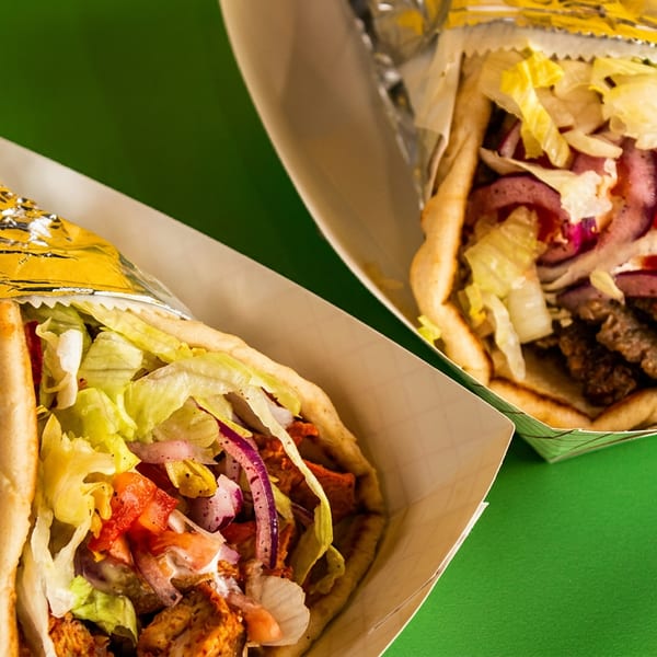 Two gyros, one chicken and one beef, in paper trays on a vibrant green background.