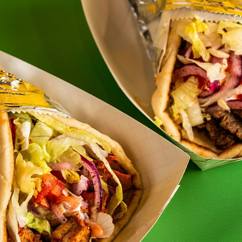 Two gyros, one chicken and one beef, in paper trays on a vibrant green background.