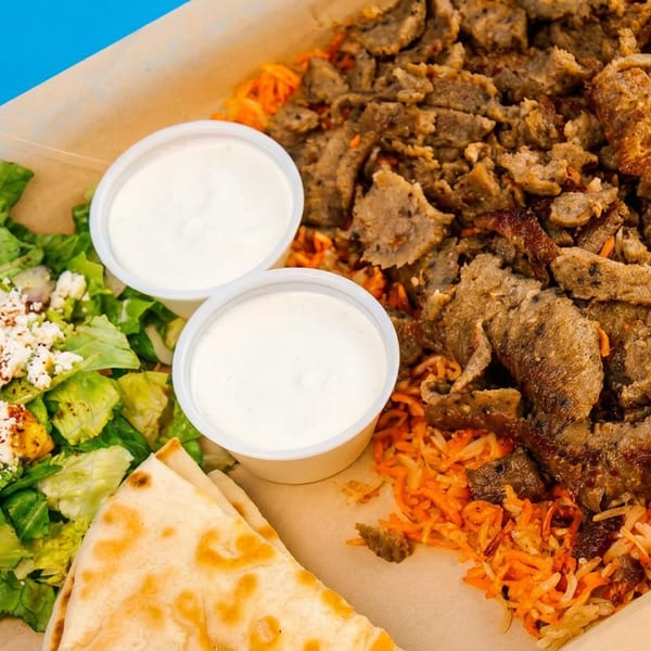 A tray with gyro meat, rice, salad with feta, two sauces, and pita bread.