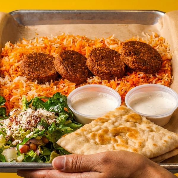 A hand holds a tray with falafel, orange and white rice, salad, pita bread, and two sauce cups.
