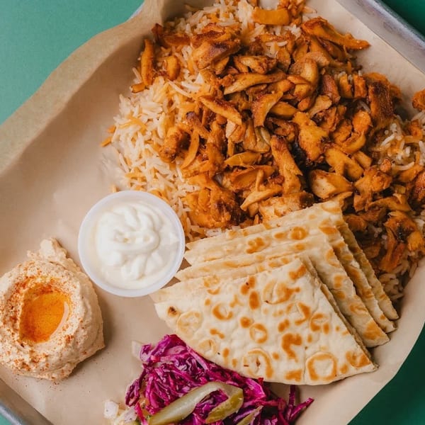 Shawarma plate with rice, chicken, hummus, pita bread, white sauce, and red cabbage salad.