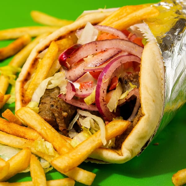 A gyros wrap with meat, red onions, lettuce, and tomatoes, surrounded by french fries.